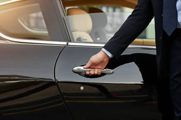 A professional chauffeur opening the door of a luxury black car, representing our Auburn Hills Airport Taxi and Limo Service for executive travelers.